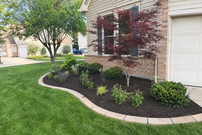 Newly installed landscape bed with shrubs, perennials, and a stone border by First Class Property Services
